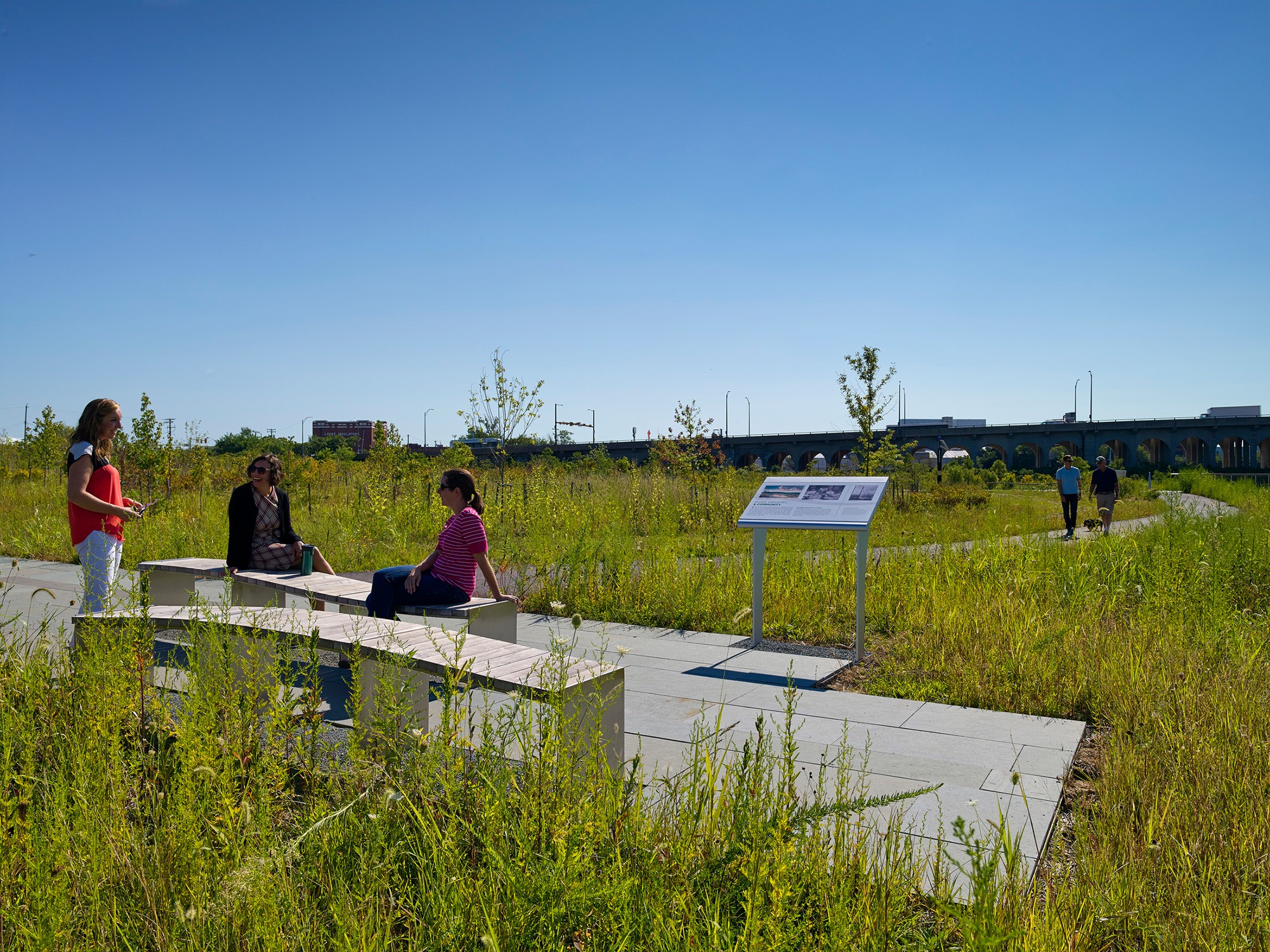 People sit on the new benches in the National Aquarium’s West Covington Park in the foreground...