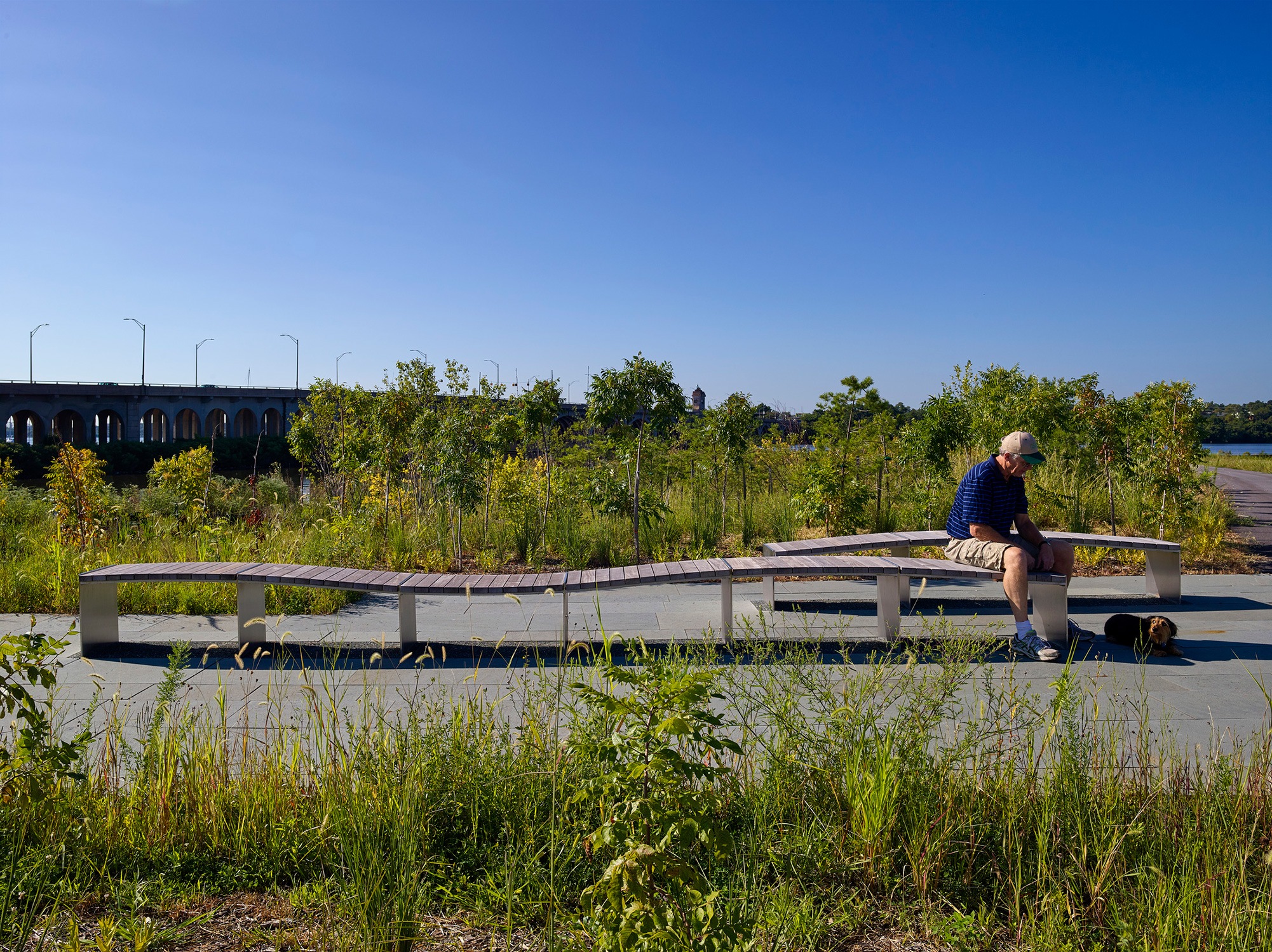 A person sits with their dog on a bench at the National Aquarium West Covington Park