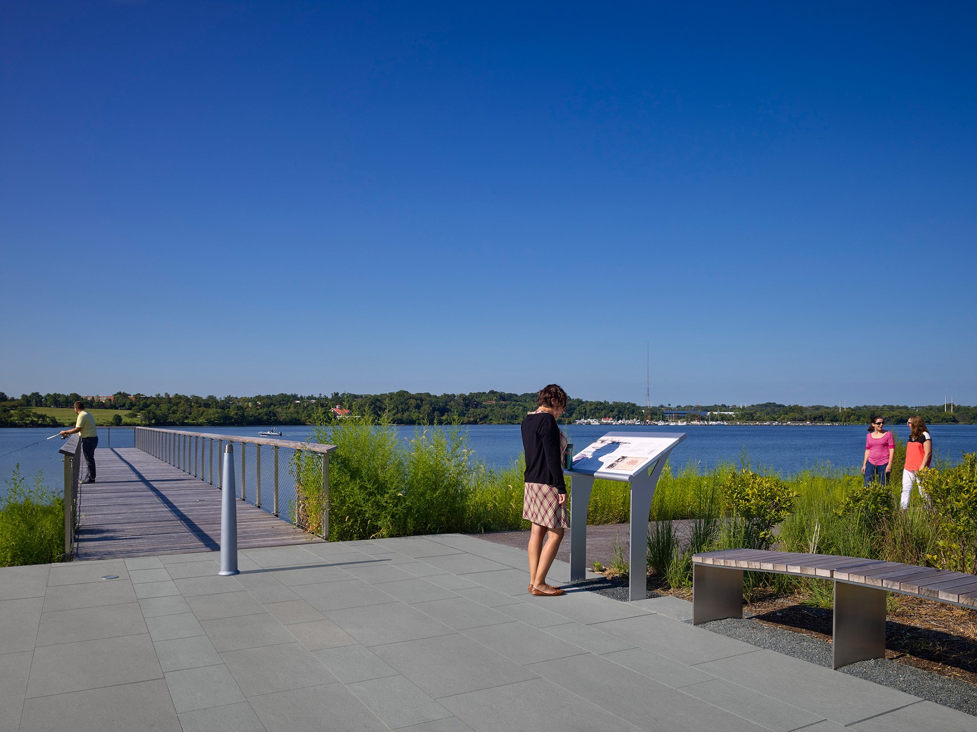 A person reads an educational sign in the foreground with the recreational pier in the background...