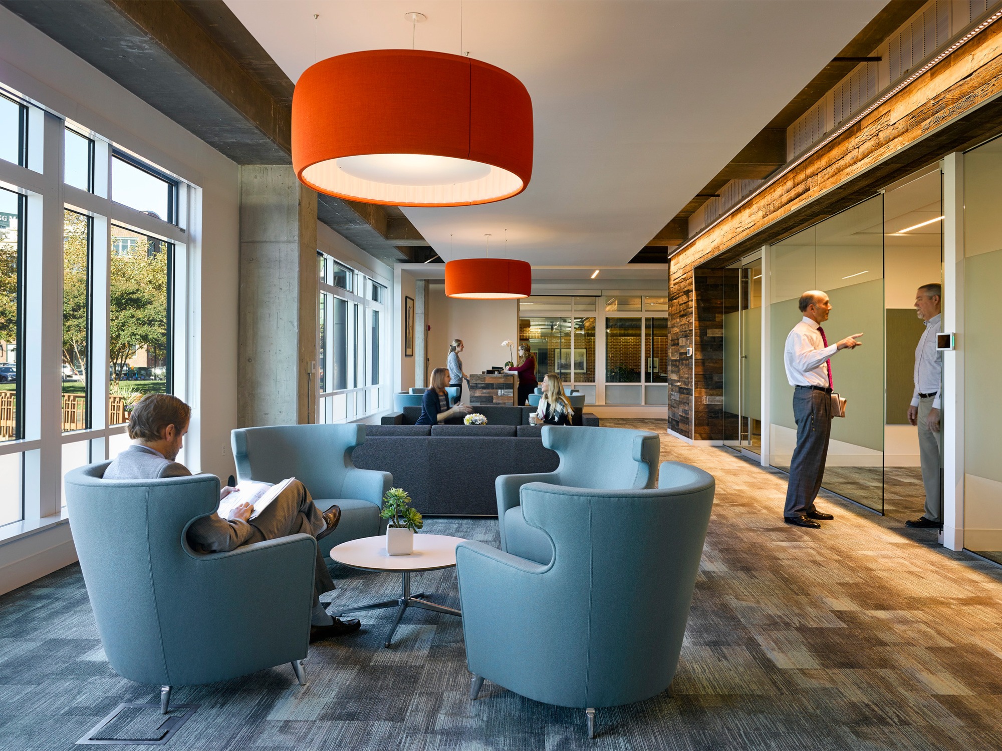 Brown Advisory lobby seating area with blue wingback chairs and orange overhead drum lights in...