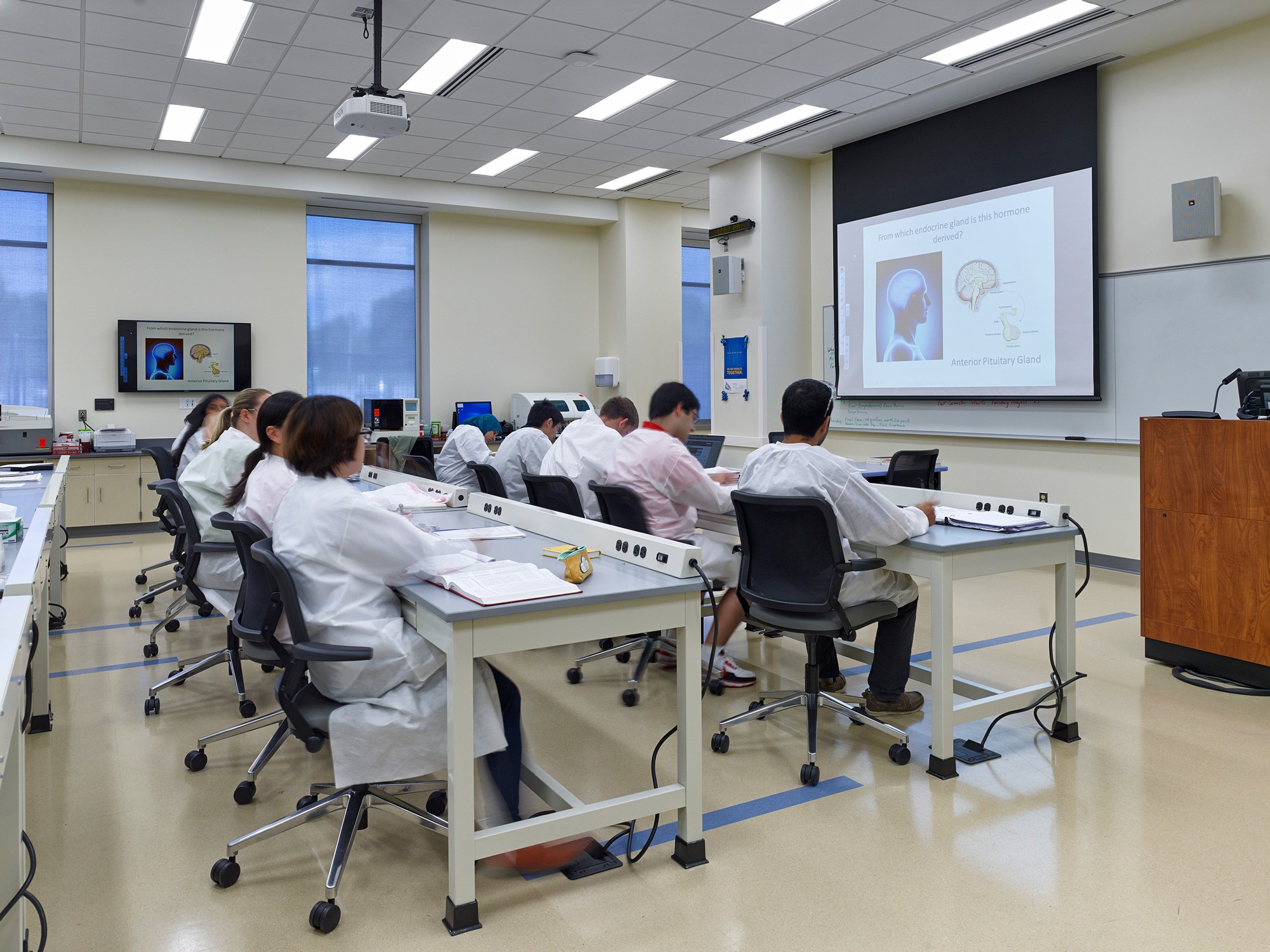 Health Science lab classroom with students in lab coats working at two rows of desks