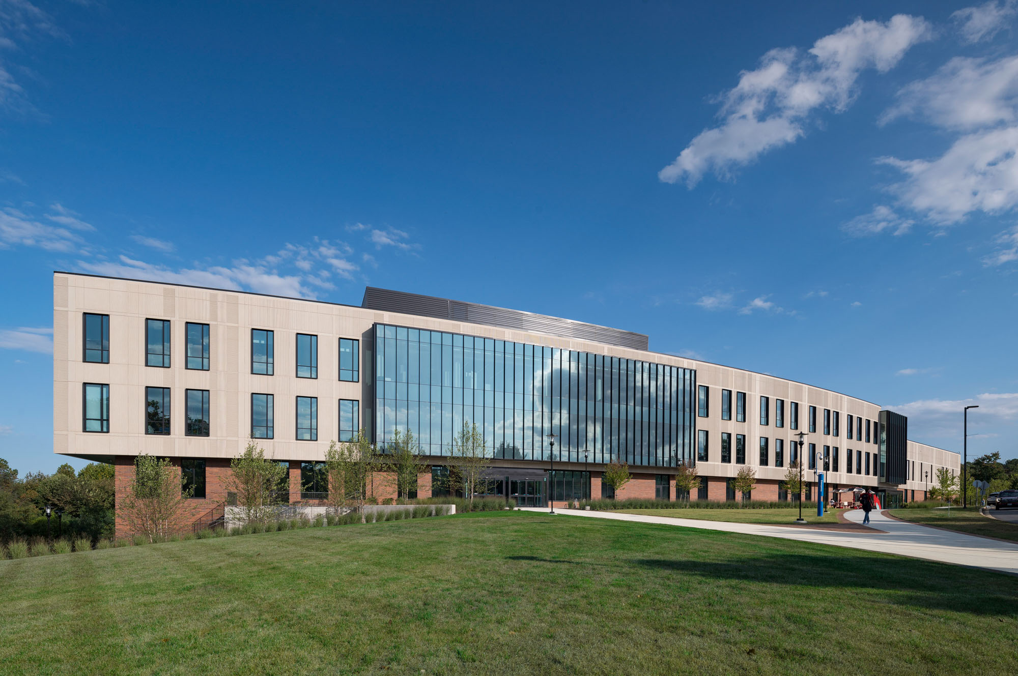 Panoramic view of modern academic building with curved glass façade, brick base, and landscaped...