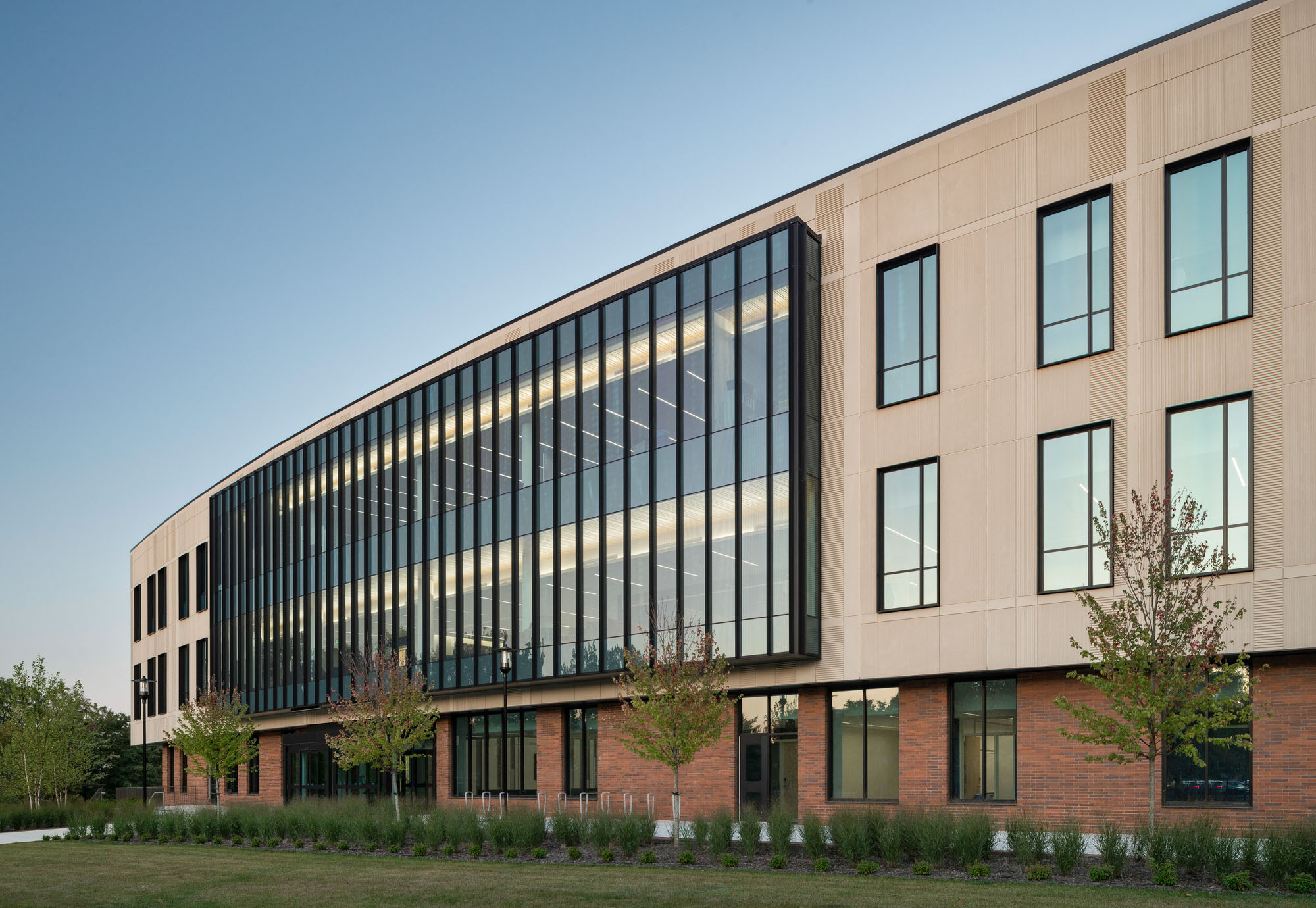 Close-up of building façade featuring tall glass panels and beige textured cladding above a brick...
