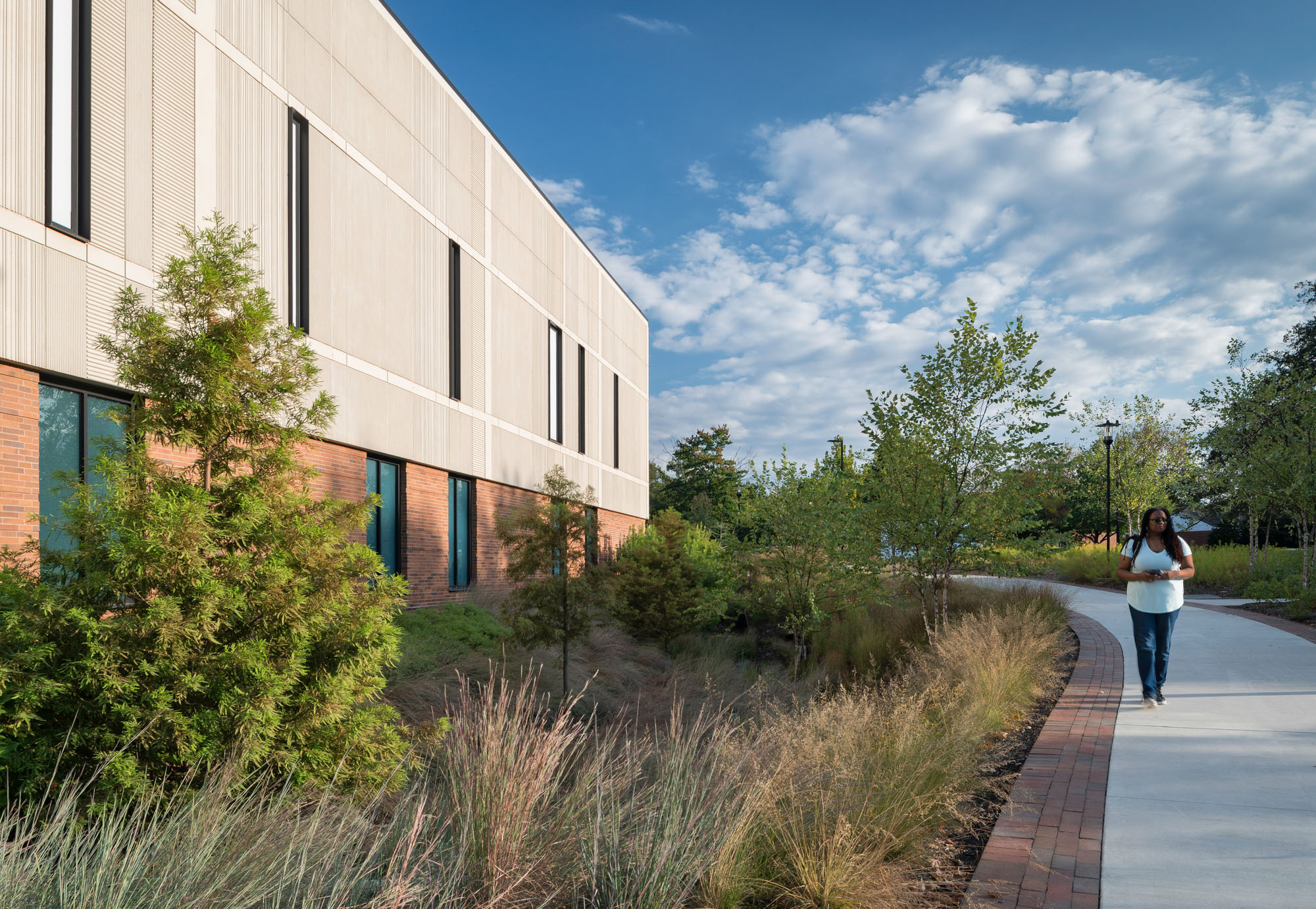 Tiered landscaping with ornamental grasses and trees in front of curved glass façade of academic...