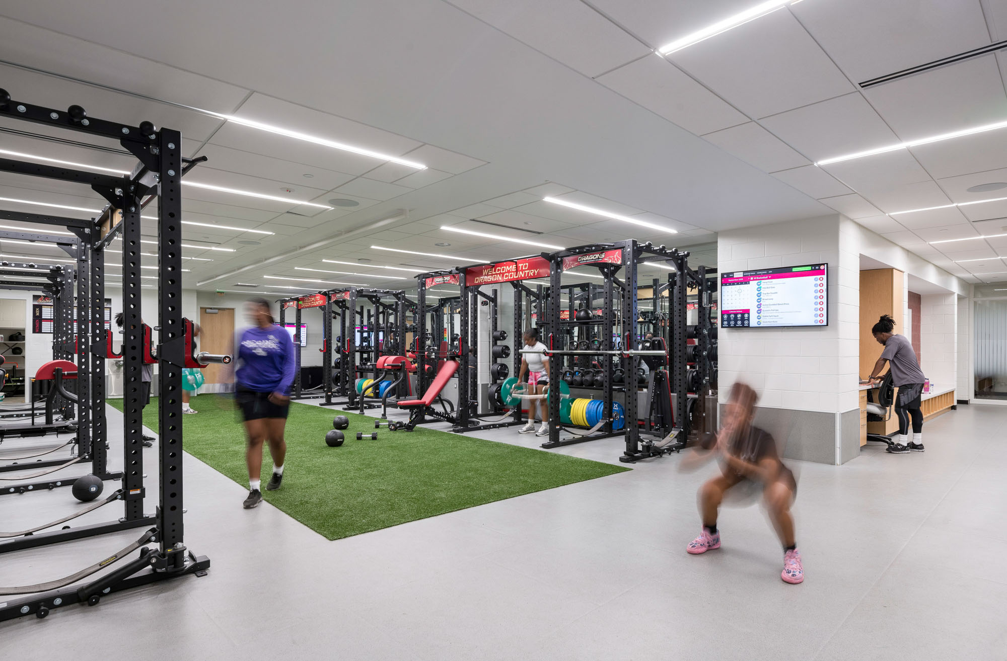 Strength training area with racks of weights, turf strip, and exercise equipment; bright overhead...