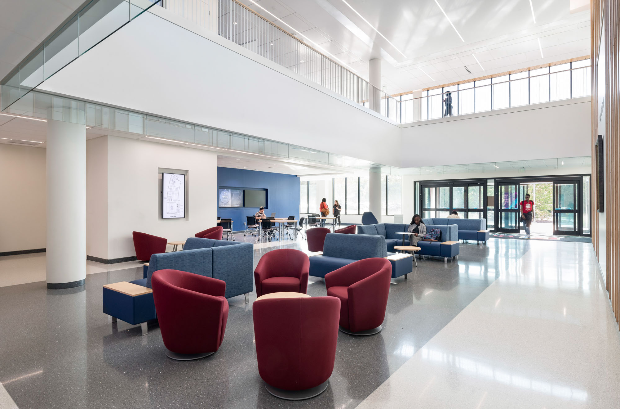 Open lounge area with natural light, red and blue seating, and tables near large windows; bright,...