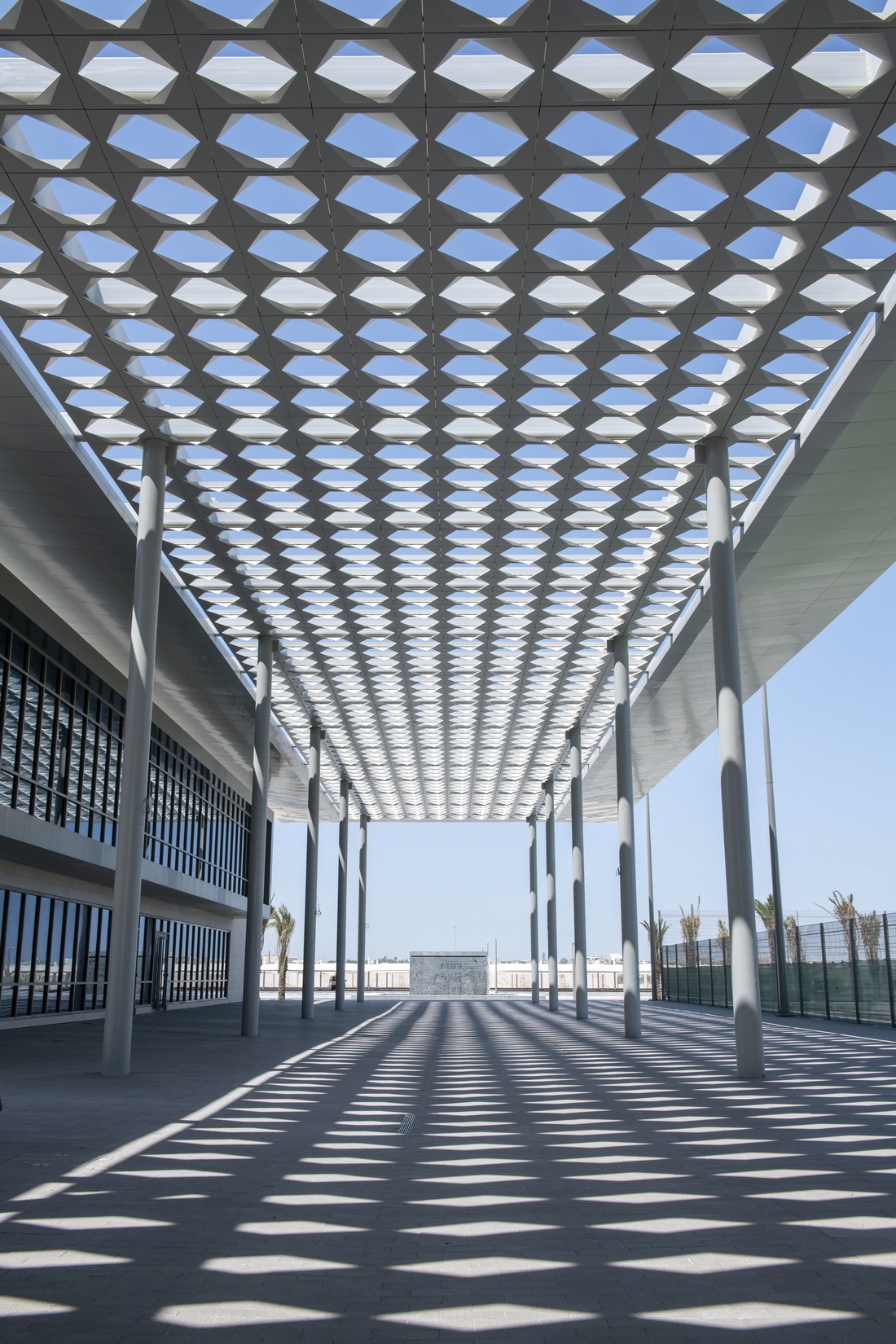 A vertical image of a walkway with geometric metal fabricated screen overhead