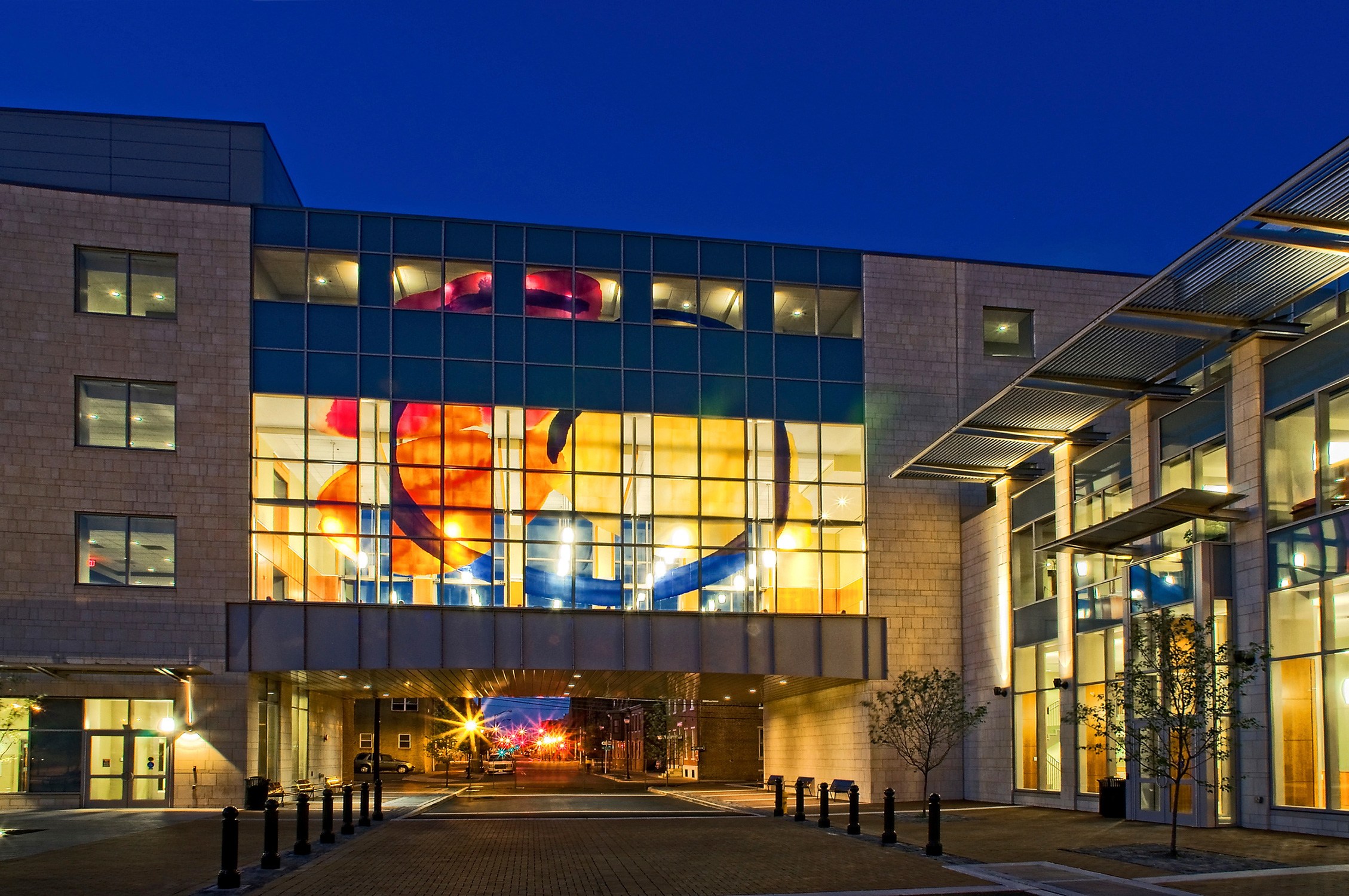Exterior dusk photo of double height student lounge with colorful windows at Rutgers University...