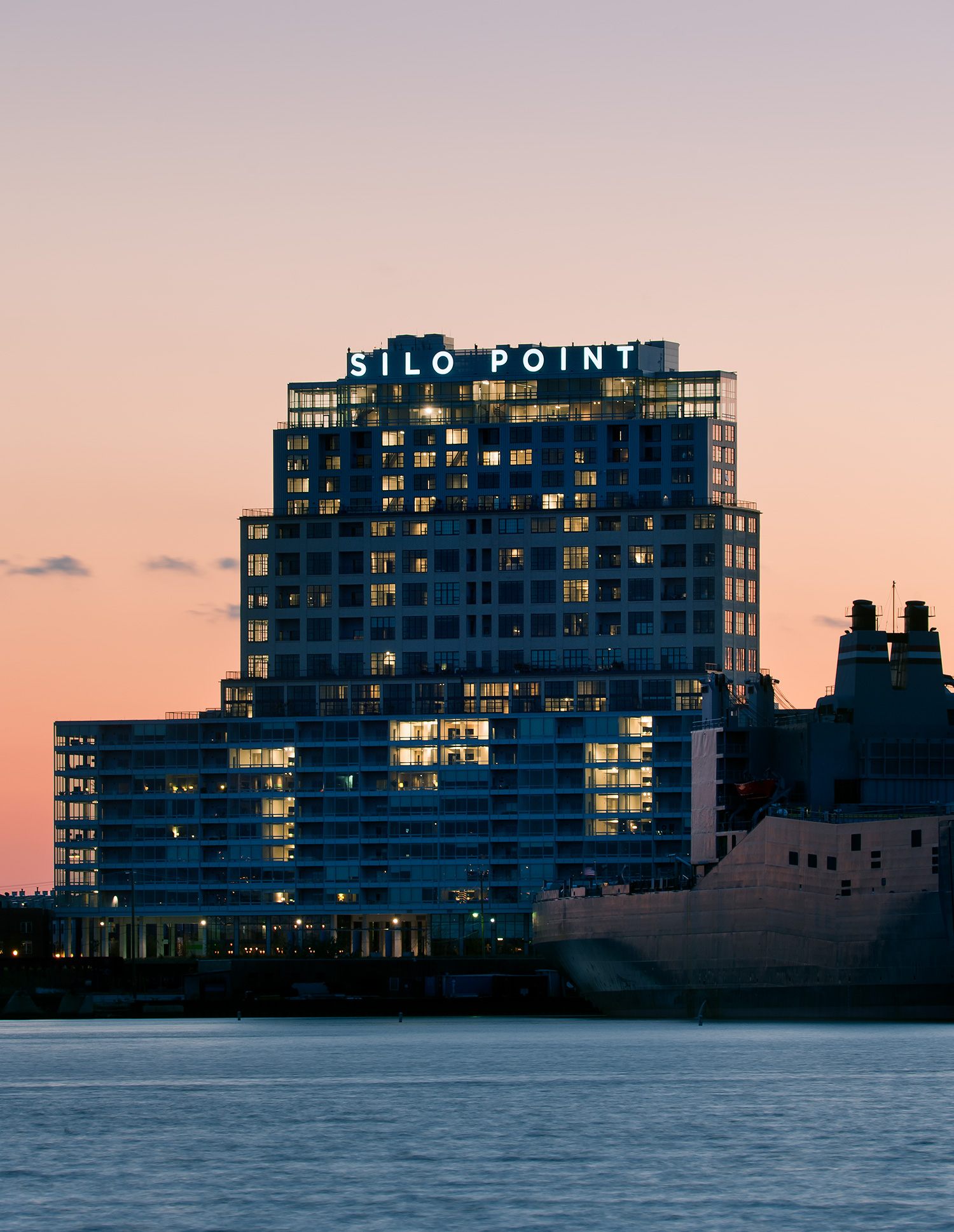 Illuminated signage at the top of Silo Point from the harbor at dusk