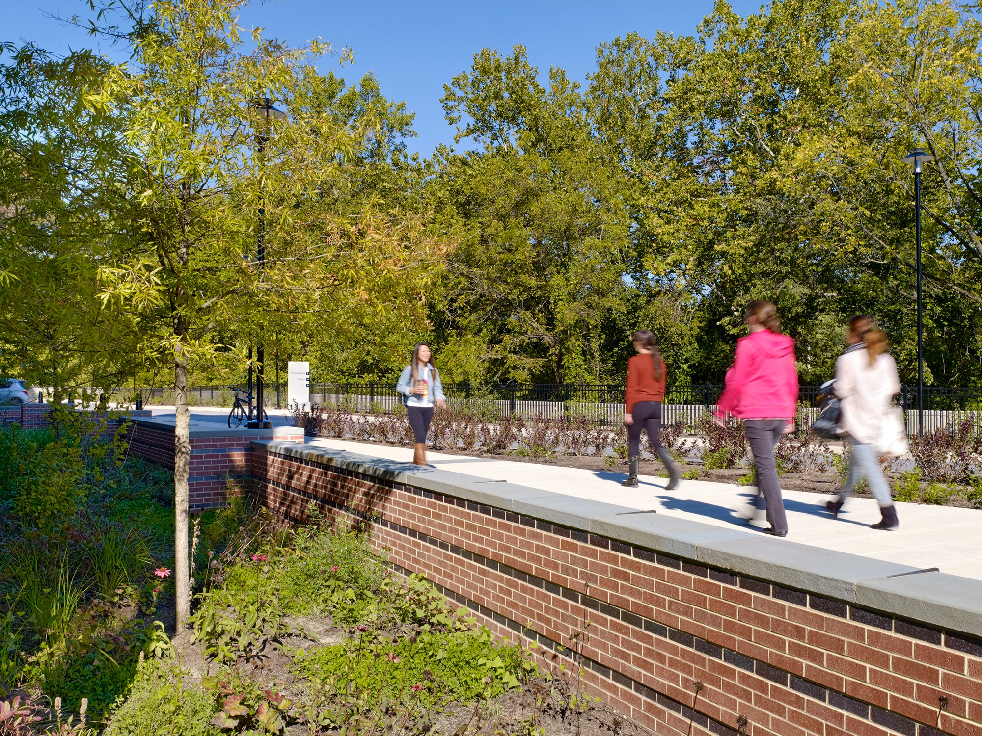 Landscaped Stormwater retention area with trees and plantings, enclosed by a brick wall with students...