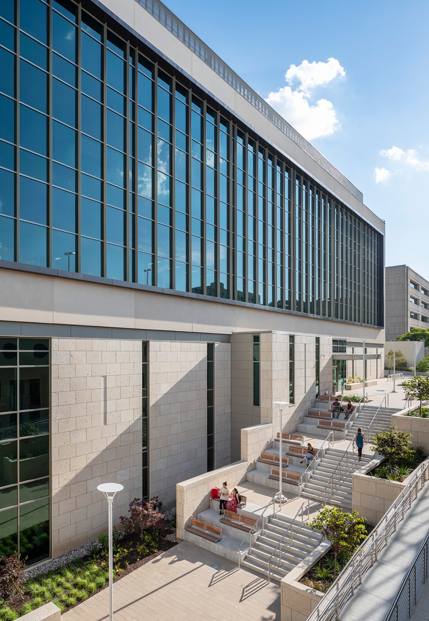 Exterior daytime image of stairs, outdoor collaboration spaces, and a wall of windows at the University...