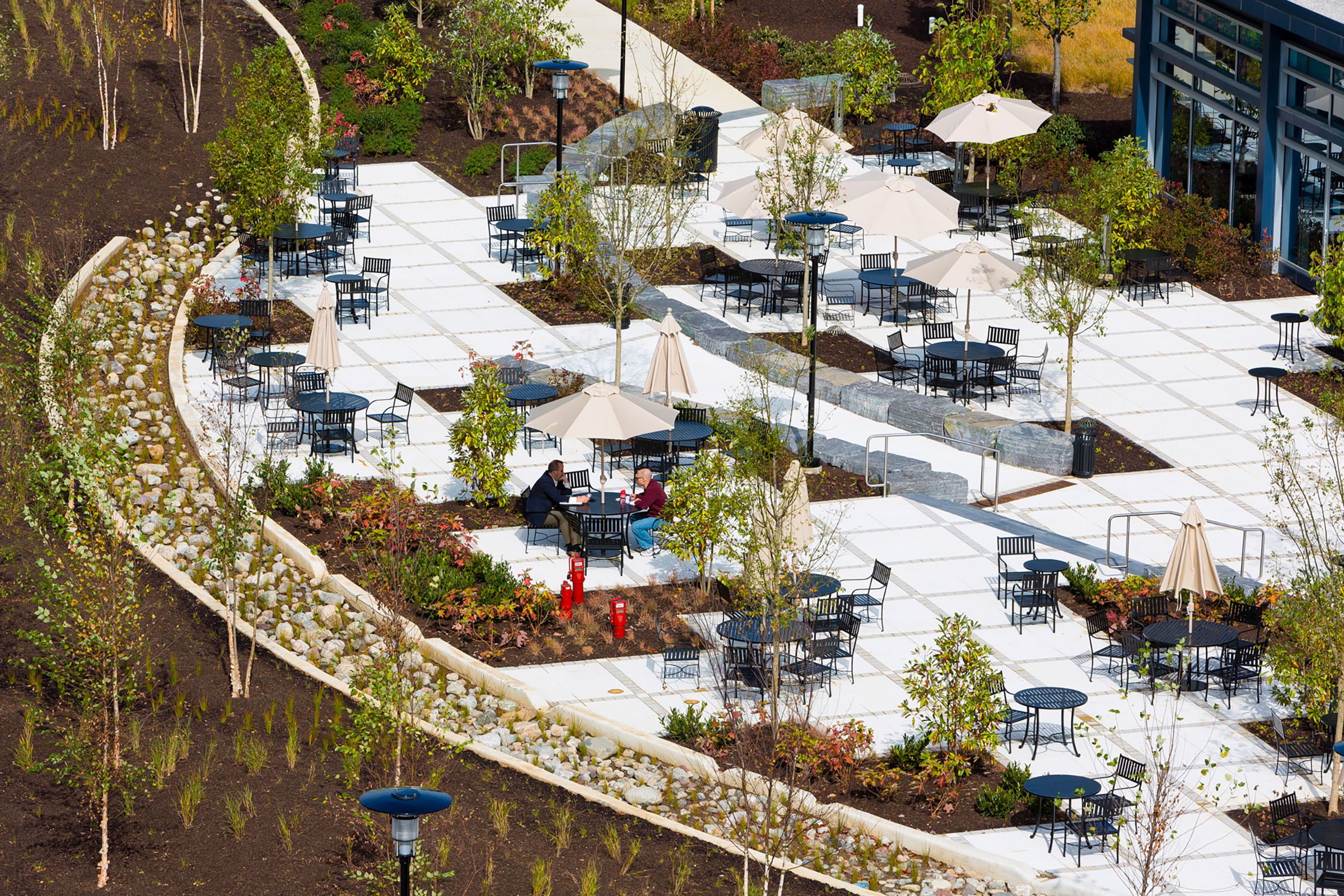 A bird’s eye view of the new dining terrace with tables, chairs, umbrellas, trees, and plantings