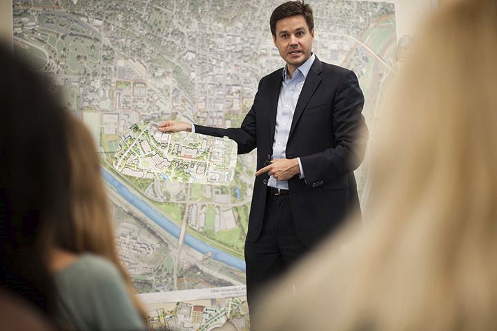 A person holding a cut out section of a plan in front of a large map and presenting to a crowd...