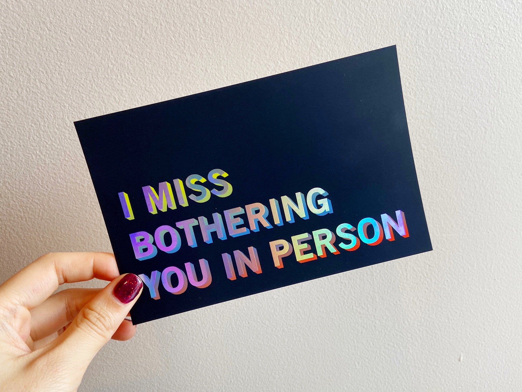 Image of a hand holding a dark blue postcard with the text “I miss bothering you in person”