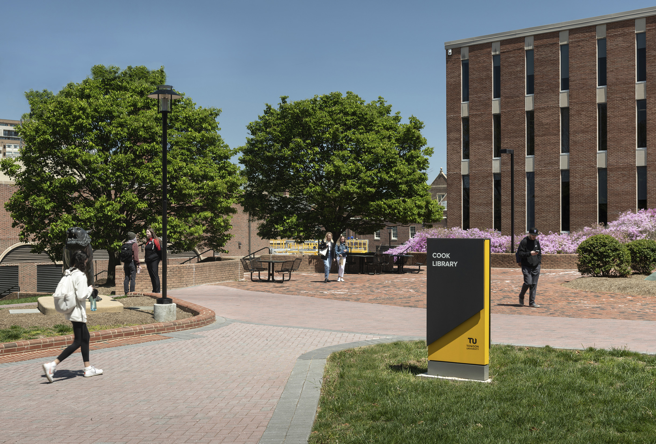 Students walk by a new sign for the Cook Library, which features an angled black panel and a gold...