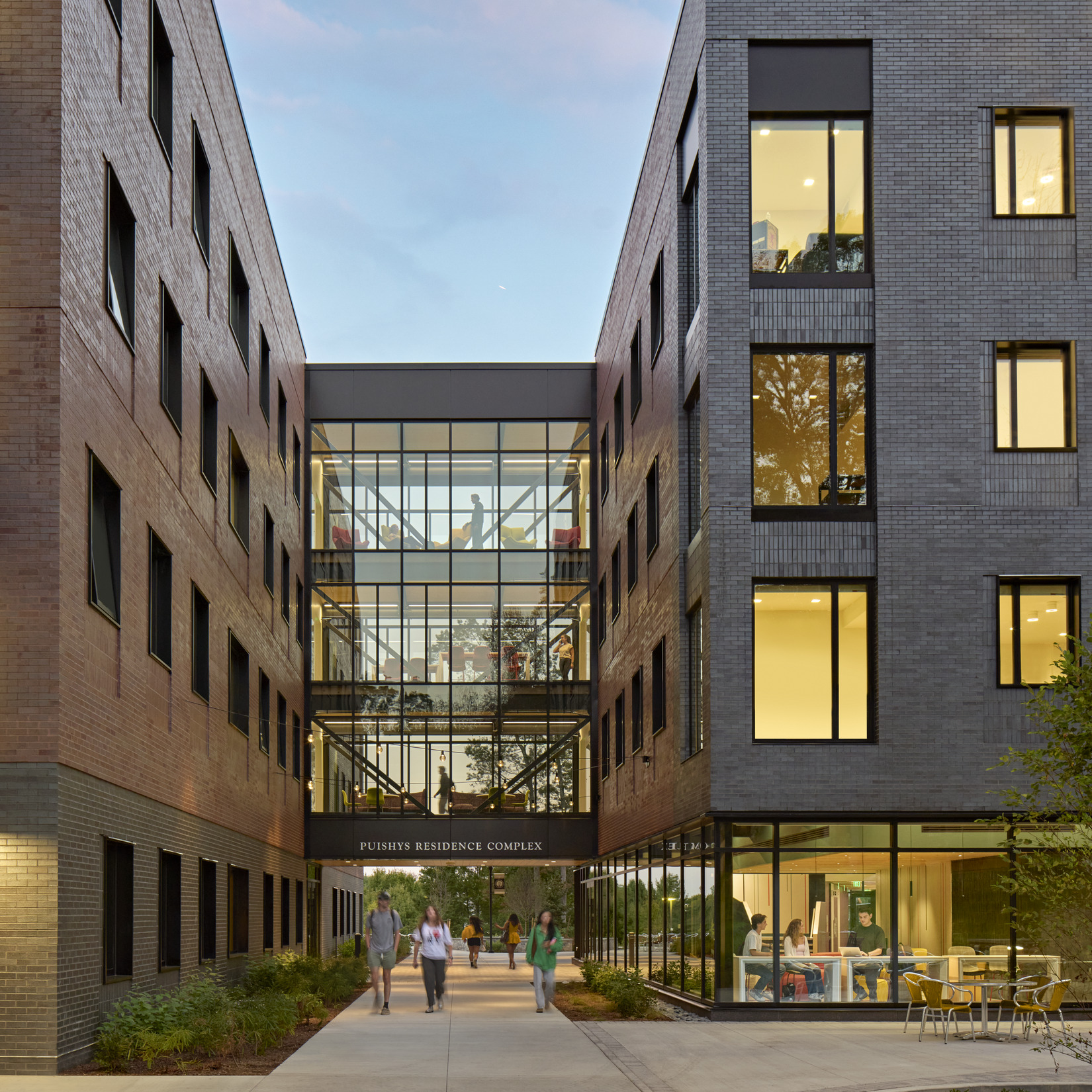A walkway runs between two tall brick buildings connected by a glass bridge. The glass structure...