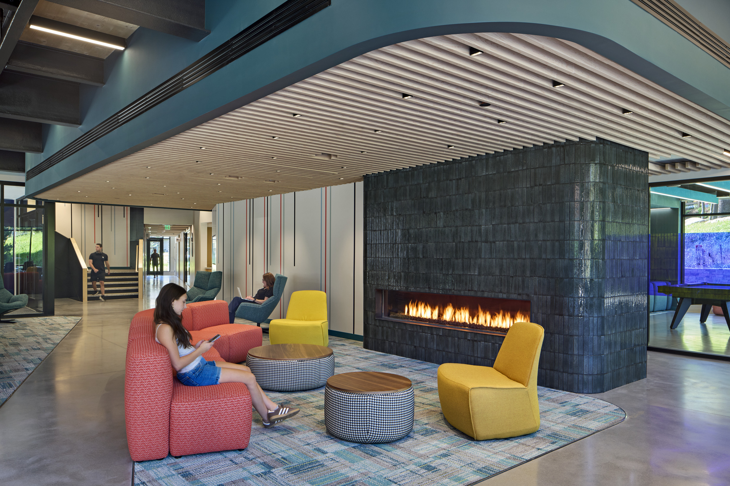 A cozy common area featuring a modern black-tiled fireplace, vibrant armchairs in red, yellow,...