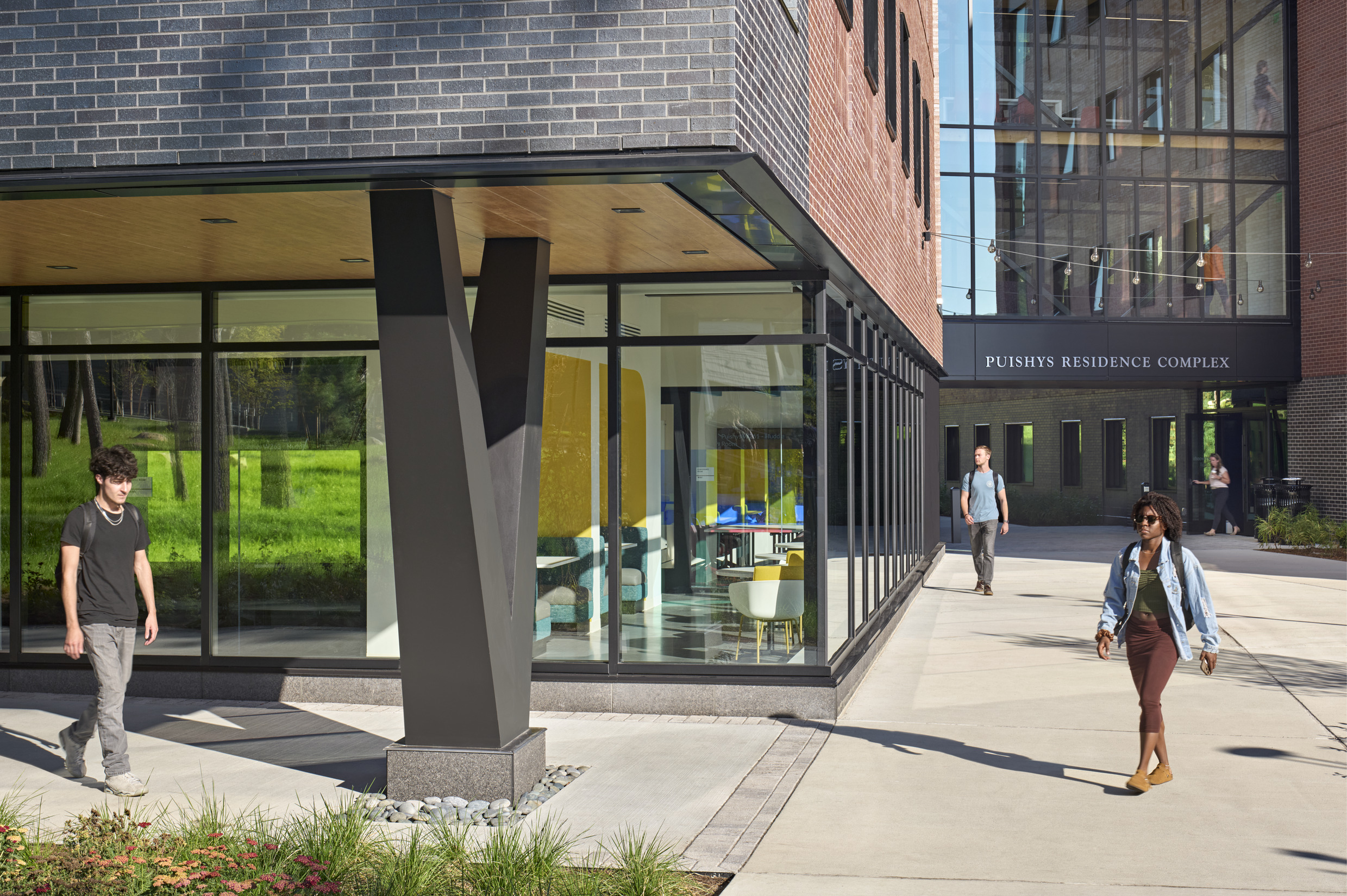 A modern building corner with large glass windows revealing a colorful interior lounge. People...