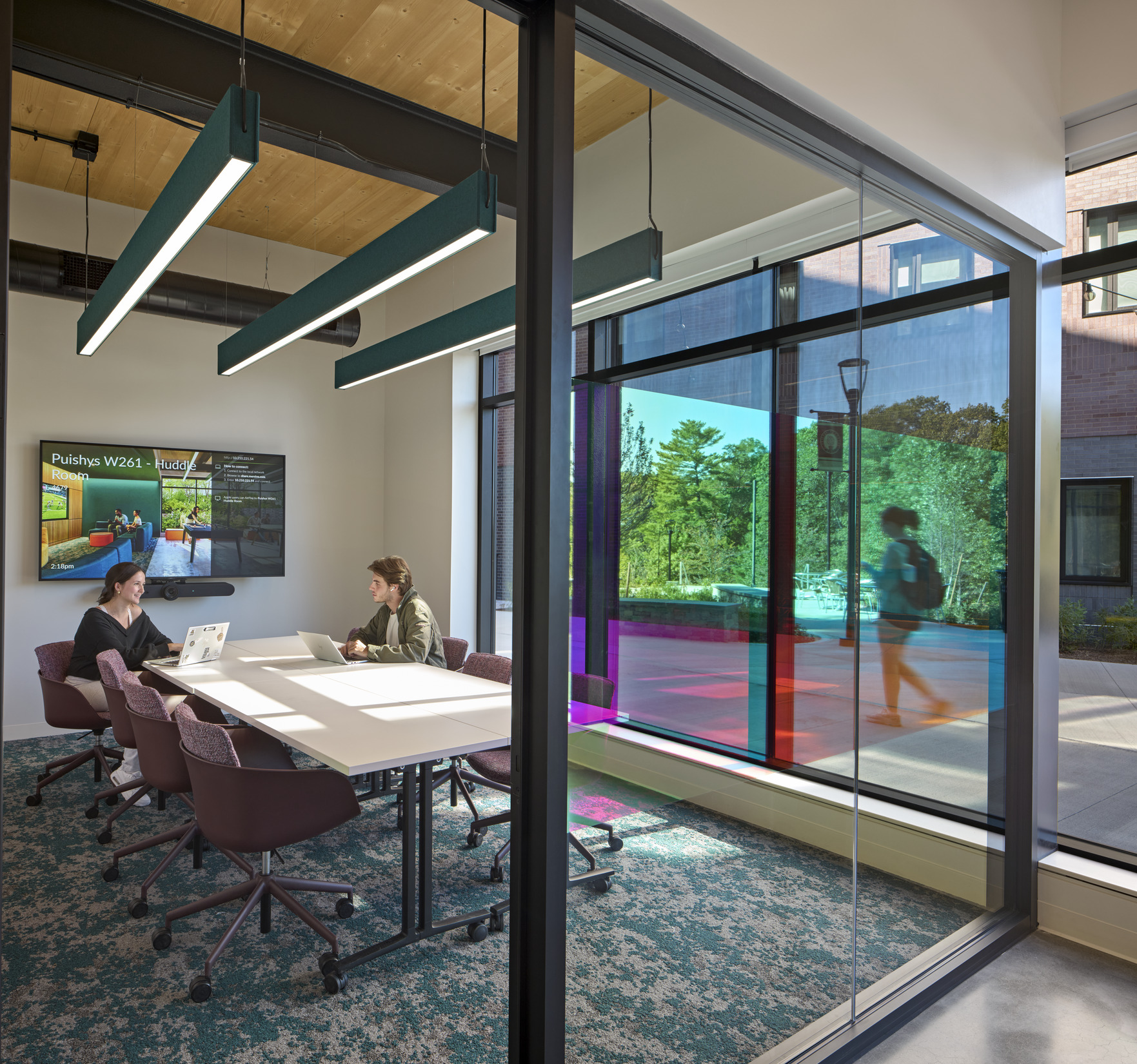 An interior space featuring a white table with purple chairs, two people working on laptops, and...