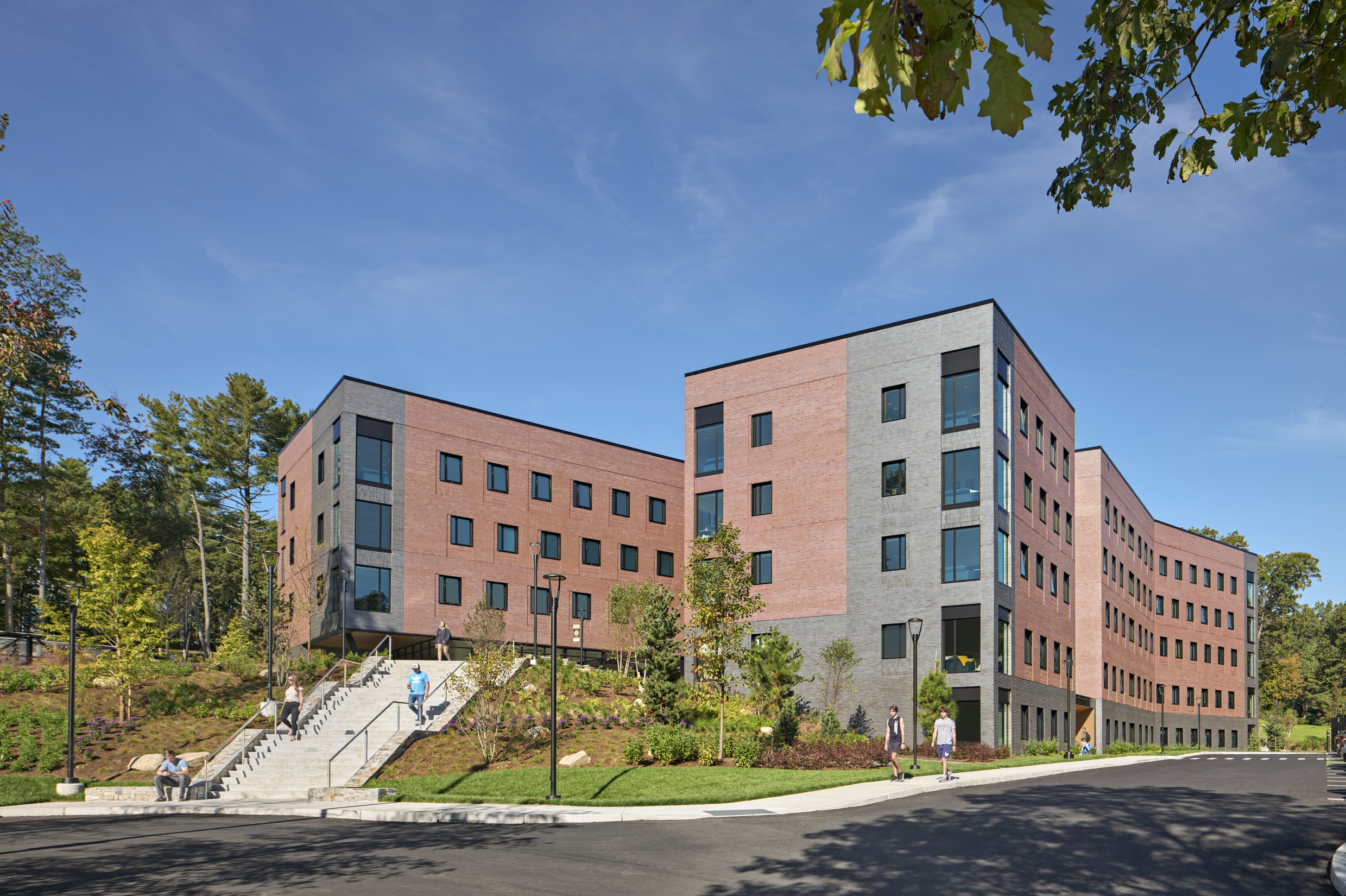A multi-story brick and gray building with large windows, surrounded by landscaped greenery and...