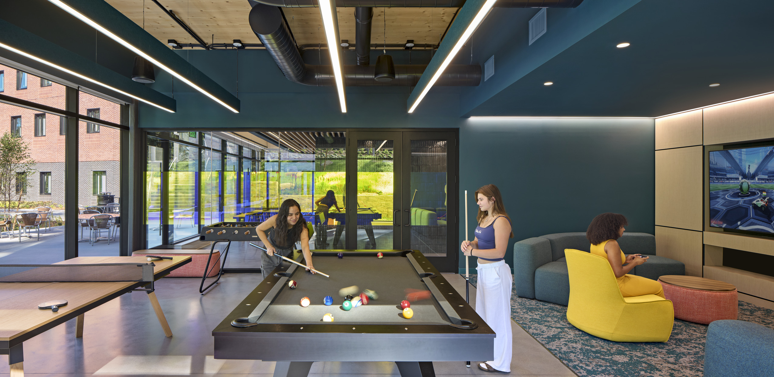 An indoor recreation space featuring a pool table, colorful lounge chairs, and a large TV mounted...
