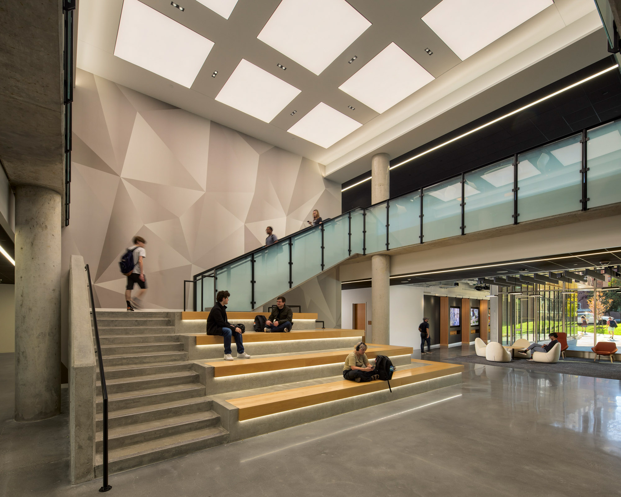 Double-height common space connects levels with a central stair and tiered seating, fostering interaction...