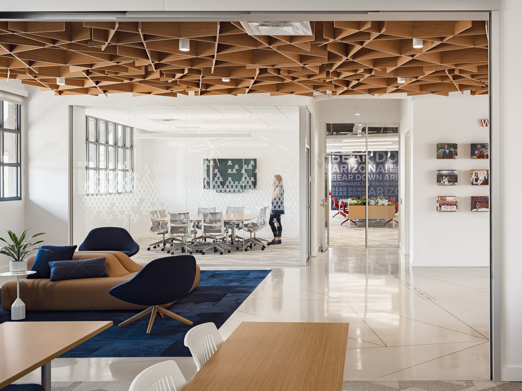 Glass-enclosed conference room and lounge area beneath sculptural wood ceiling feature.