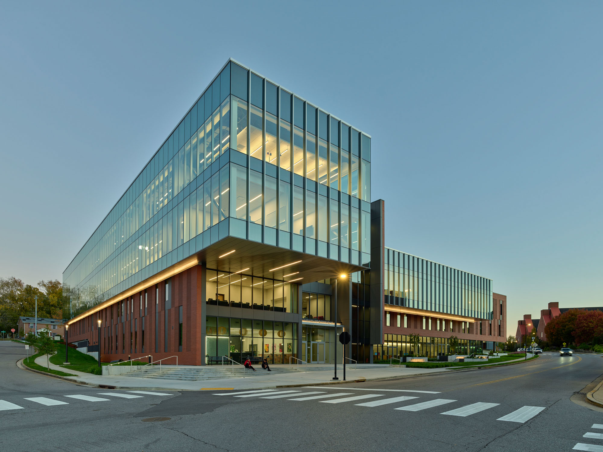 Health Professions Building at twilight, featuring a cantilevered glass upper level and warmly...