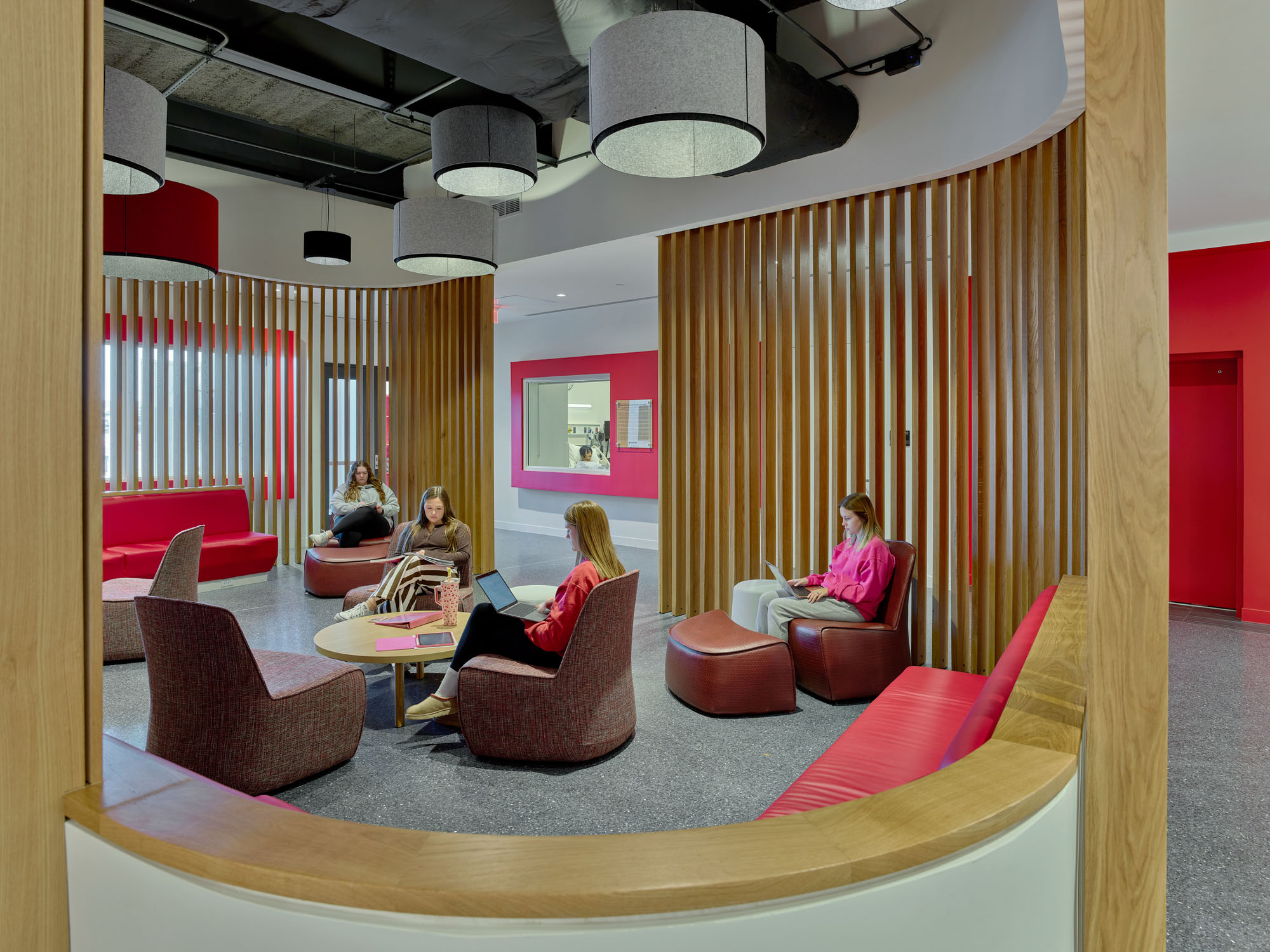 Students study in a vibrant collaboration lounge with wood slat partitions, soft seating, and bold...