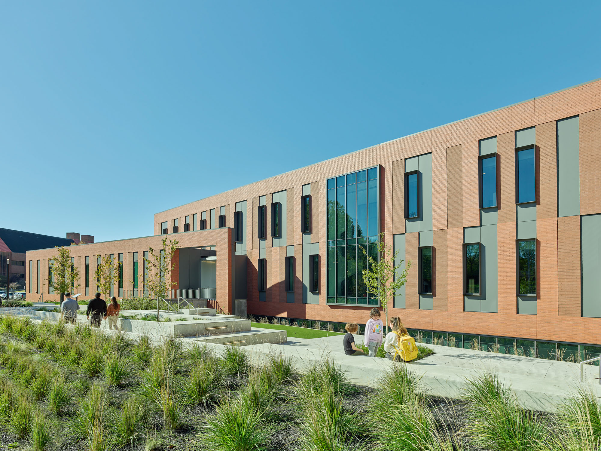 Students sit and walk along landscaped pathways with native grasses and concrete seating adjacent...