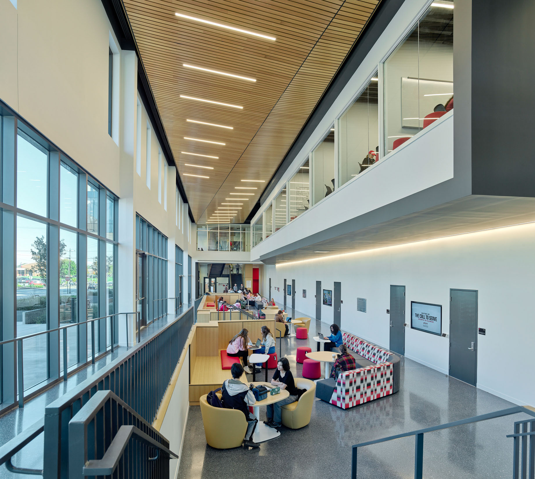Students study and meet in a two-story collaboration area with floor-to-ceiling windows, wood slat...