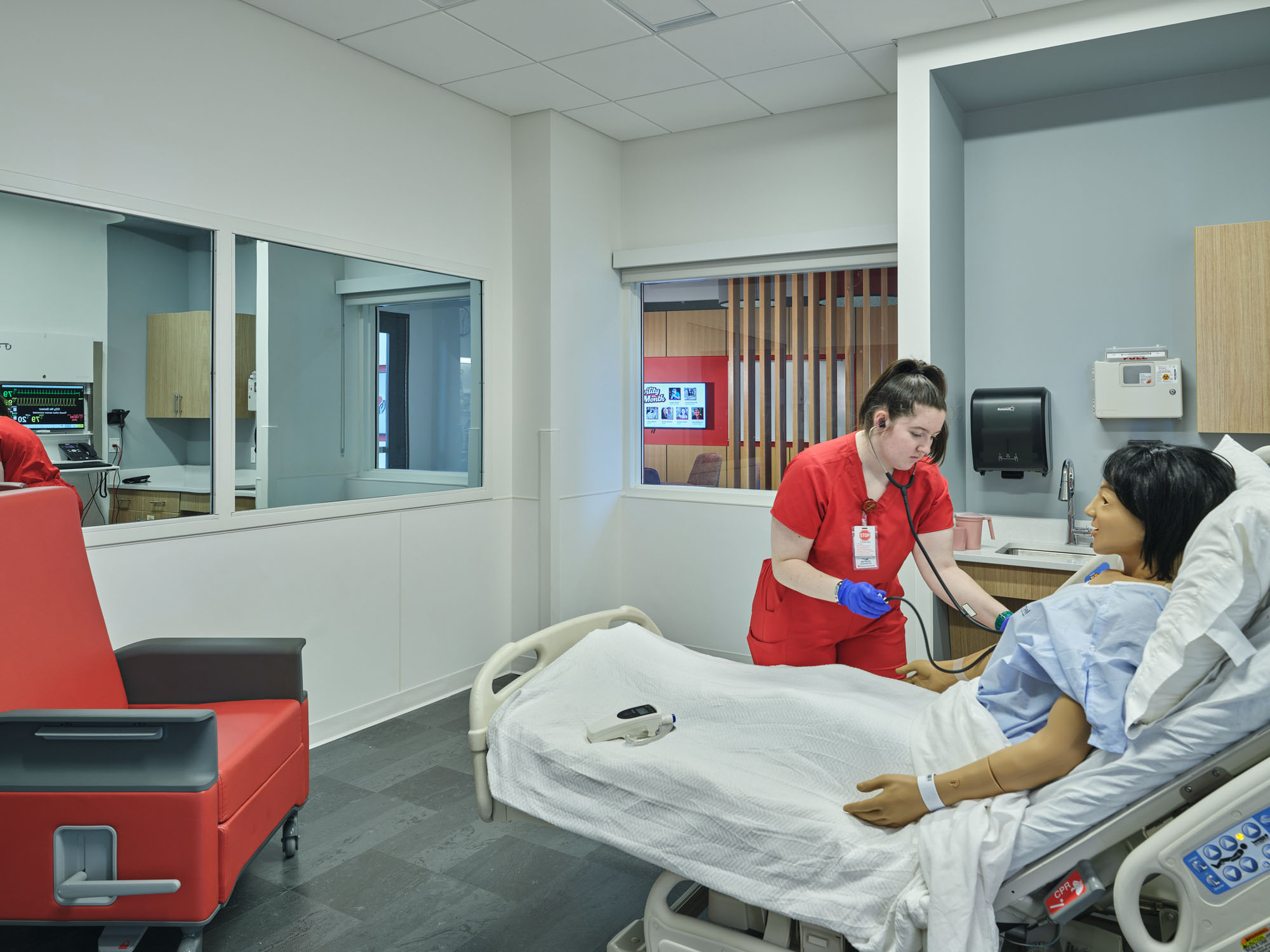Nursing student practices patient care skills in a clinical simulation room with a hospital bed...