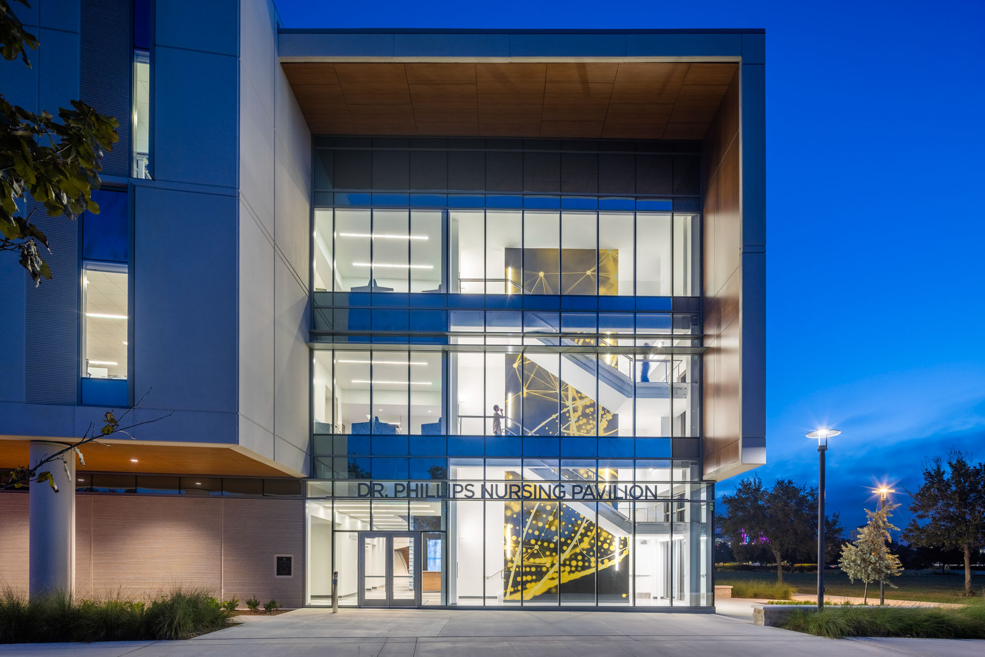 Nighttime exterior of the nursing pavilion lobby with visible interior activity and people moving...