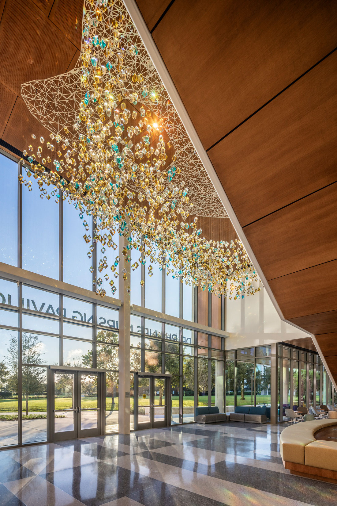 Light-filled lobby with glass stair, wood accent wall, and suspended sculptural installation in...