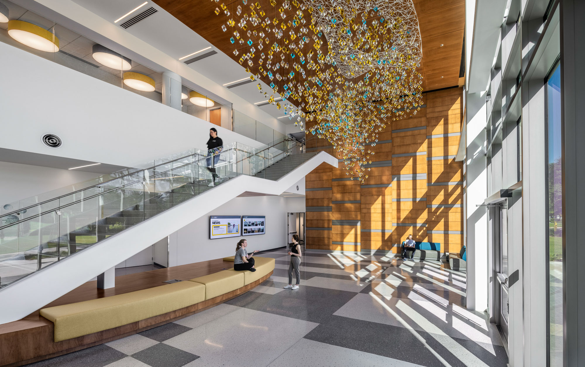 Light-filled lobby with glass stair, wood accent wall, and suspended sculptural installation in...