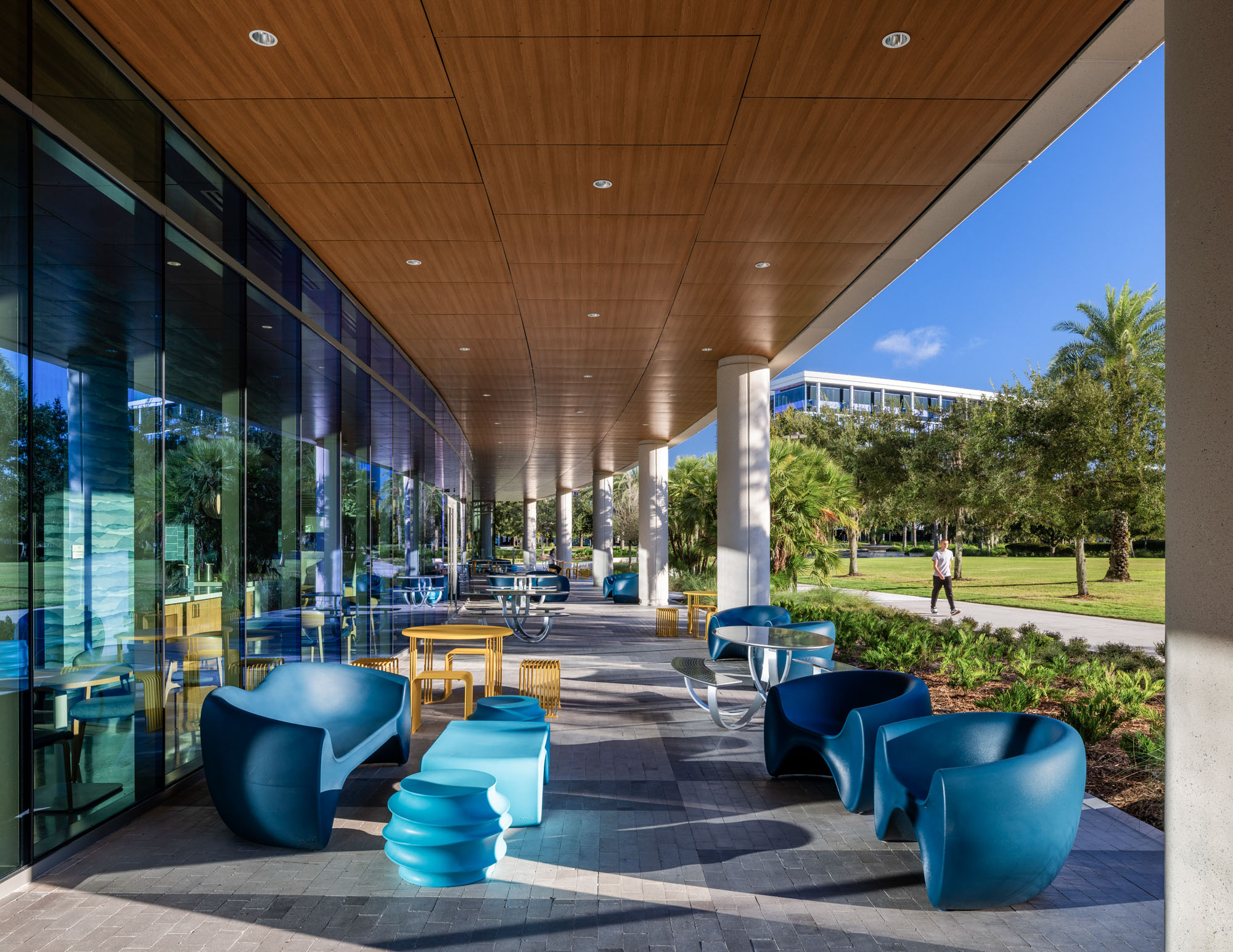 Covered outdoor patio with modern seating and tables adjacent to landscaped campus grounds.