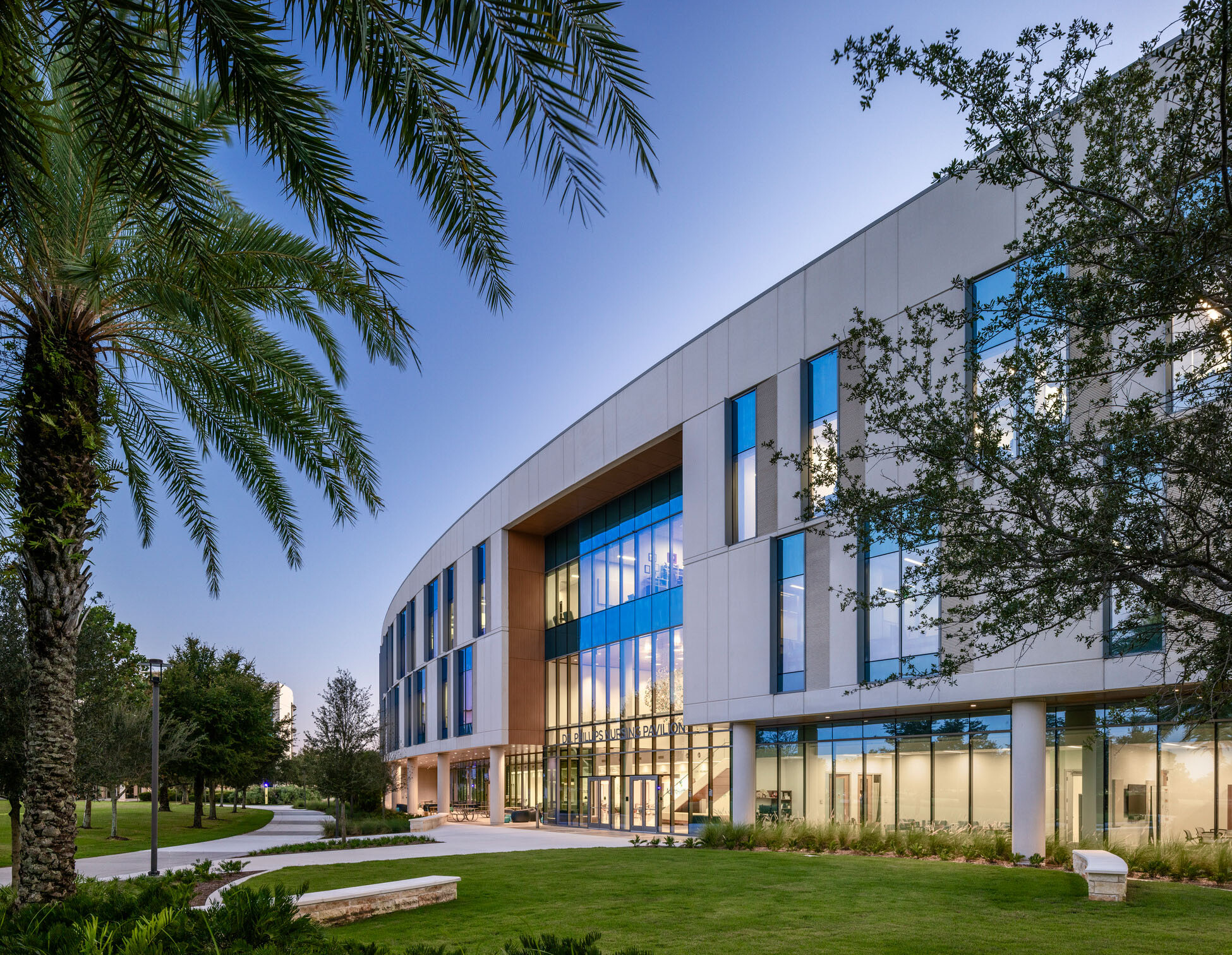 Exterior view of the curved nursing pavilion framed by palm trees and landscaped pathways.