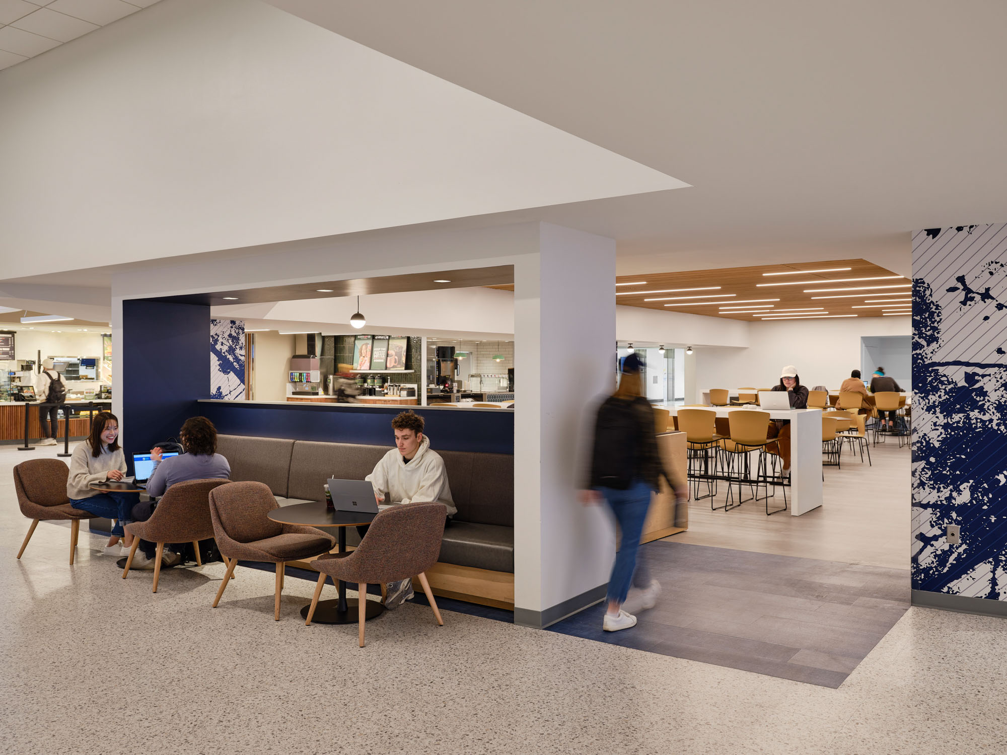 A university dining space features mixed seating including upholstered lounge chairs, a built-in...