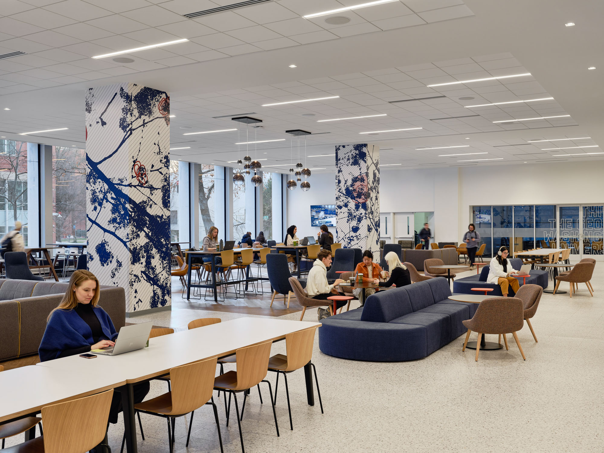 A bright university student commons features a warm wood slat ceiling with integrated linear lighting....