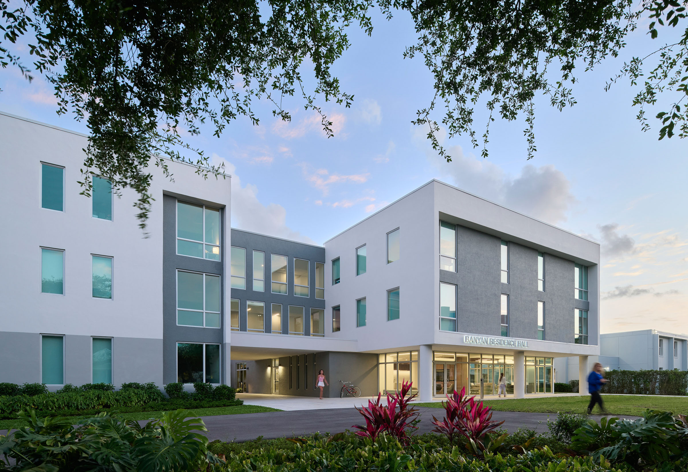 Dusk exterior view of the Banyan Residence Hall entrance at Lynn University. The three-story building...