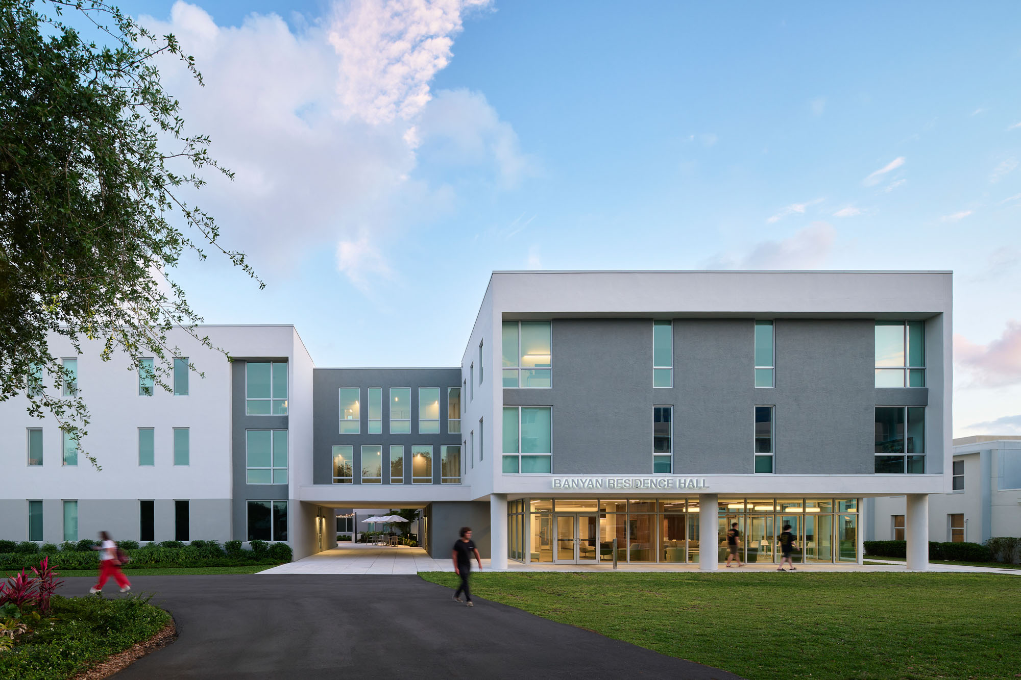 Wide dusk exterior view of Banyan Residence Hall showing the full entrance composition. The three-story...