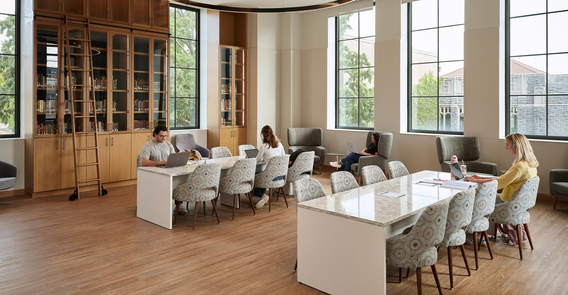 Students study at long stone tables in a room with wooden display shelves at The Catholic University...
