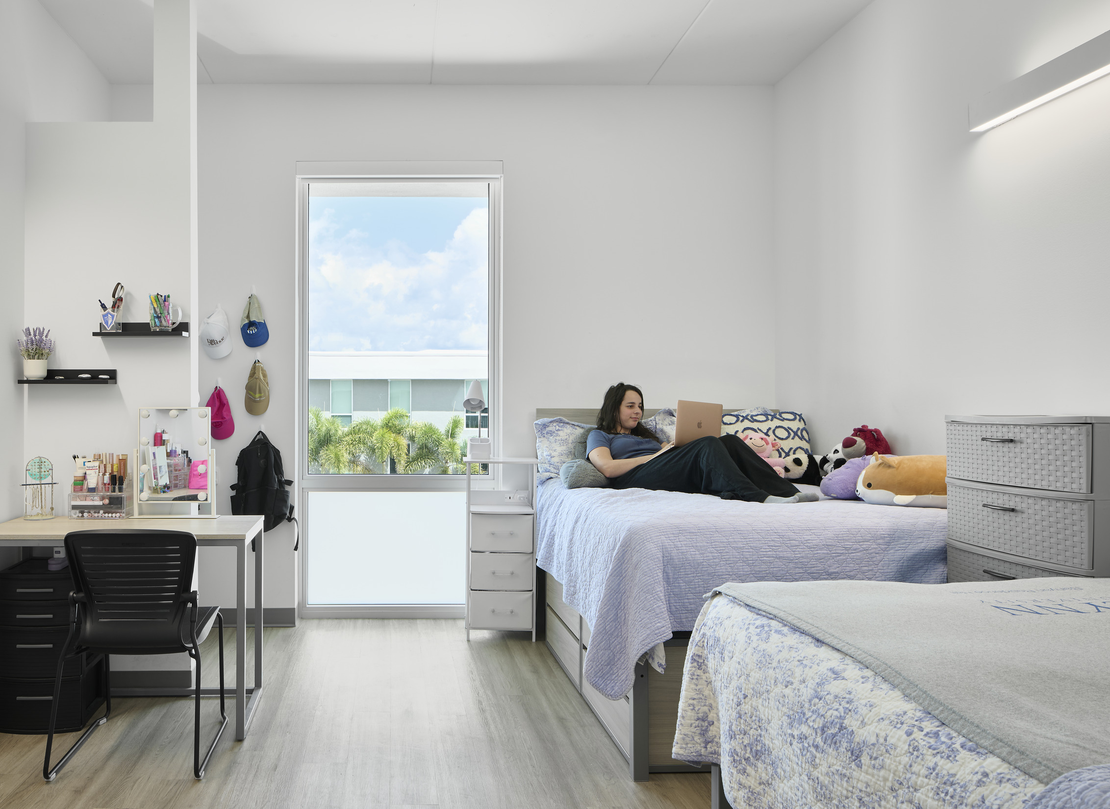 A student reclines on a bed in a shared living space at Banyan Residence Hall.